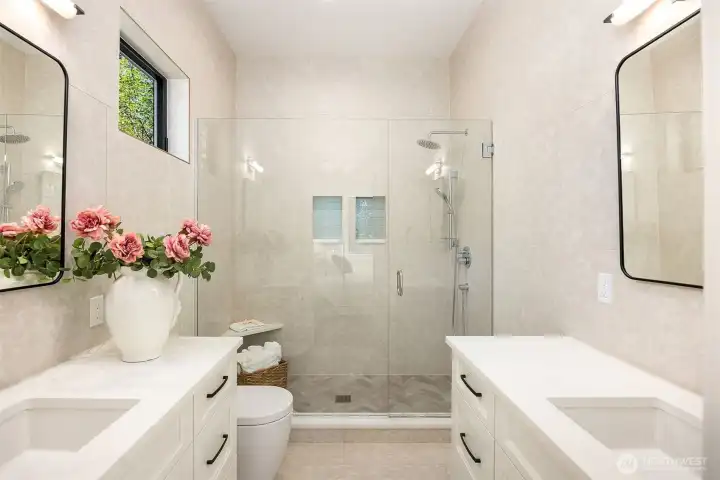 Main level ensuite: Attached bathroom with sliding barn door entry offers two separate vanities, each with its own sink, Floor-to-ceiling ceramic tile, Glass front walk-in shower with dual shower plus built shower niche