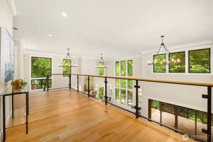 Magnificent floating I-Beam staircase with wood treads and glass panels opens to an expansive landing and wide hallway overlooking the peaceful woodland outlook and the great room below.