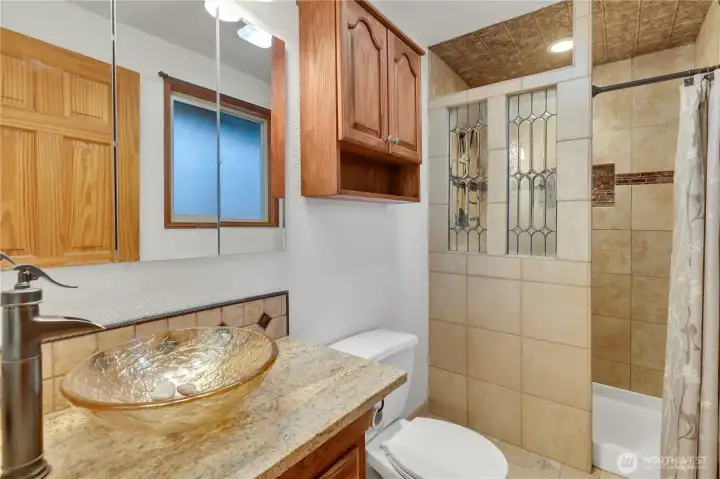 The primary bath has warm tile and a glass sink...