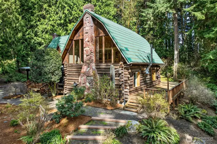 A rare handcrafted log home set against a cathedral of Pacific Northwest evergreens — this iconic A-frame silhouette with green tile roof and soaring brick chimney delivers the kind of curb presence you simply cannot replicate.