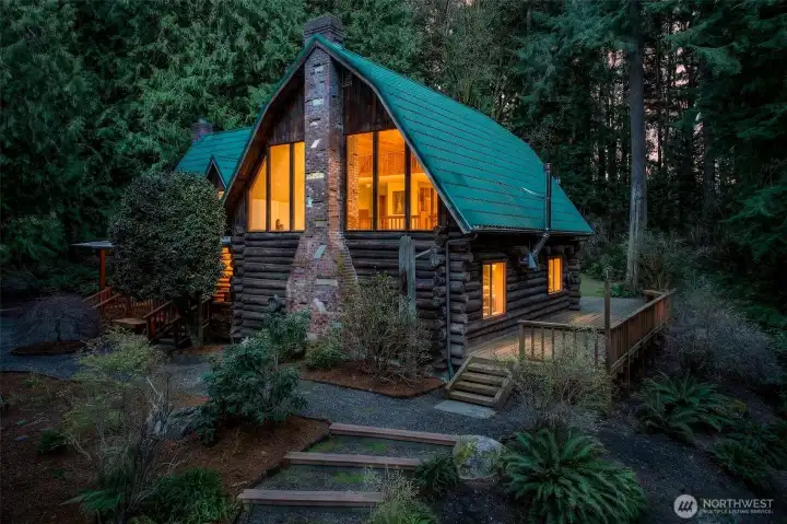As evening settles in, the home glows from within — warm light pouring through the soaring gable windows creates a magical, storybook atmosphere that makes arriving home feel like an escape from the world.