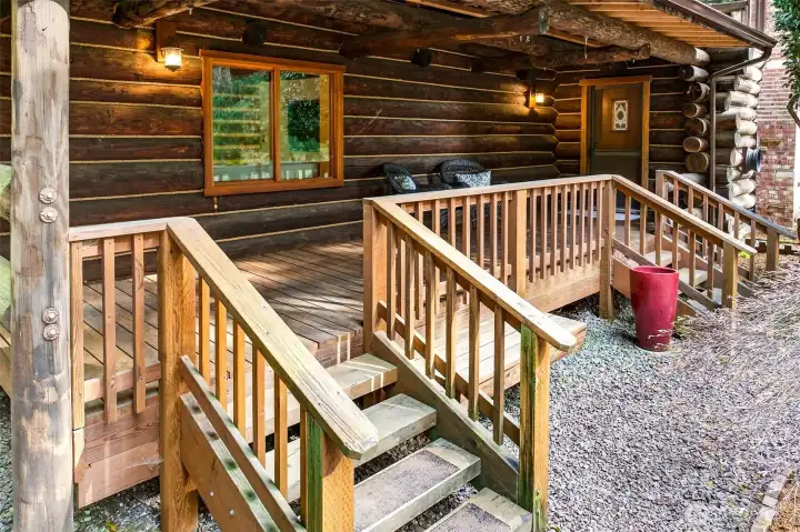 The covered front porch offers a protected outdoor living space year-round — a perfect spot to enjoy the sights and sounds of the surrounding forest, with exposed log beam ceilings overhead and hand-crafted detail at every turn.