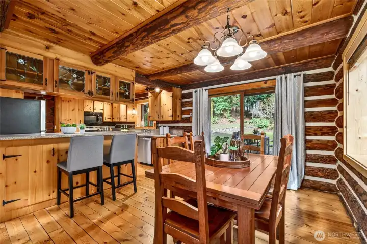 The updated kitchen and dining area blend rustic charm with everyday functionality — knotty pine cabinetry with leaded glass accents, quartz counters, stainless appliances, and a dining space opening to the forested backyard make this the true heart of the home.