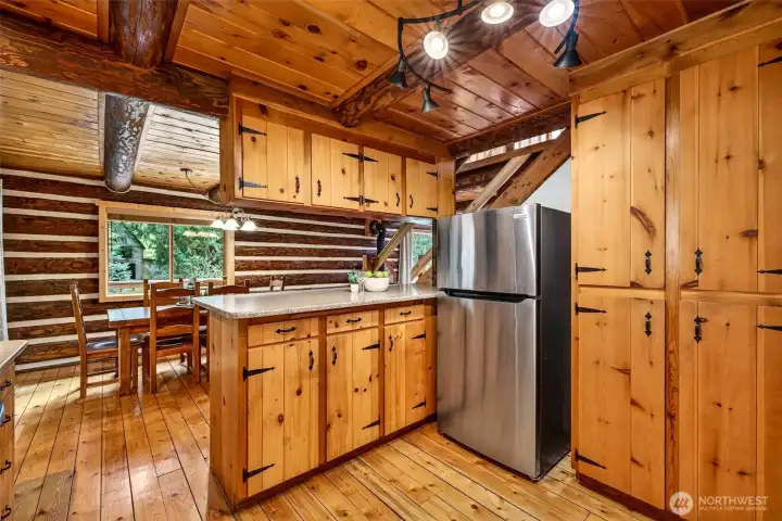 Generous storage, a spacious peninsula, and a direct sightline to the dining area give this kitchen outstanding everyday livability — the open layout keeps the cook connected to the rest of the home while the forested views beyond add a sense of calm.