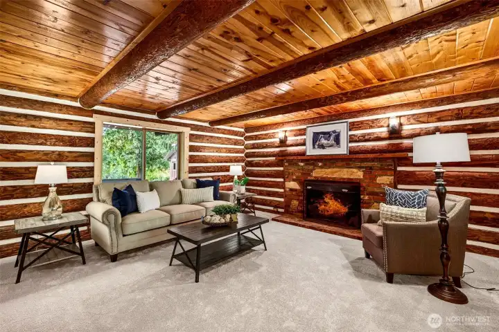 A second living space on the main level offers incredible flexibility — log walls, exposed timber beam ceilings, a brick fireplace with stone surround, and garden views create a room that works equally well as a family room, media room, or quiet retreat.