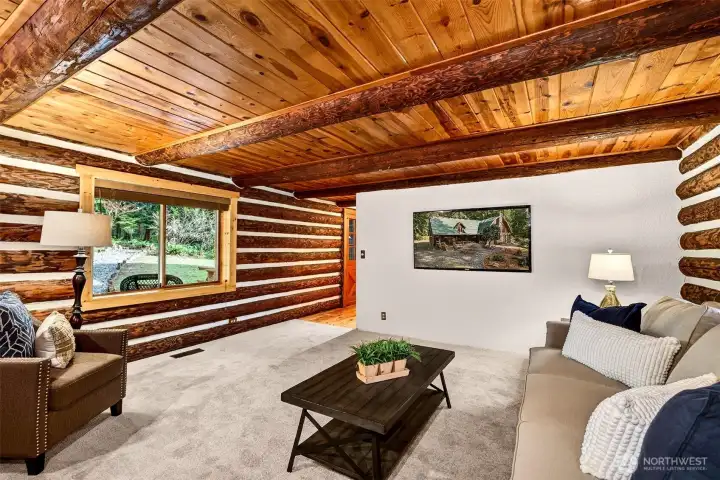 With log beam ceilings, handcrafted log walls, and a large picture window framing the forested grounds and detached garage beyond, this versatile lower-level room offers the ideal setup for a media lounge, playroom, or casual gathering space.