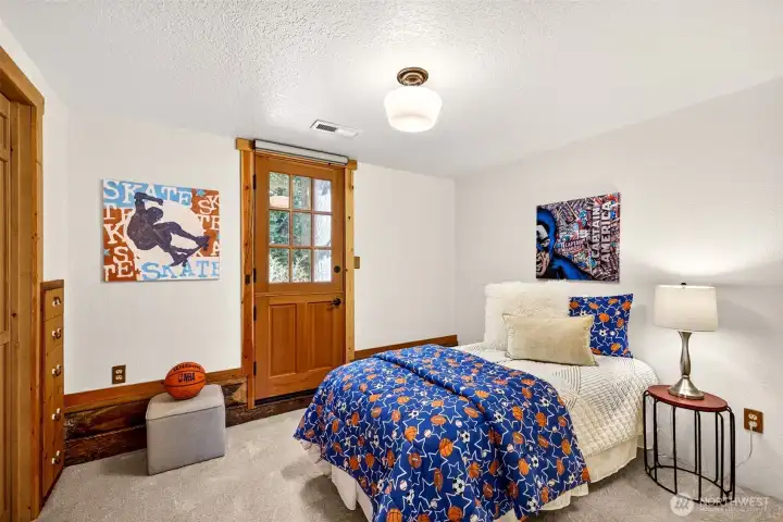 Secondary bedroom with a charming Dutch-style interior door, private deck access, closet storage, and a forested window view offers a versatile space that works equally well for guests, a home office, or a hobby room.