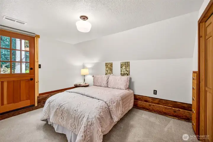 The third bedroom is a comfortable and private retreat — with an angled ceiling, private deck access, a forest-view window framed in warm wood trim, and closet storage, it adapts easily to guests, a dedicated workspace, or additional sleeping quarters.
