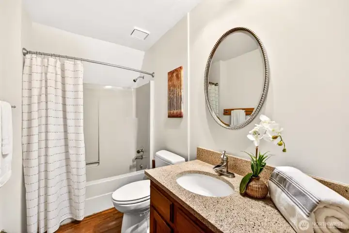 The updated full hall bath serves the secondary bedrooms with clean, thoughtful finishes — granite countertop, warm wood cabinetry, a tub and shower combination, and a generous vanity make it practical and welcoming for everyday use.