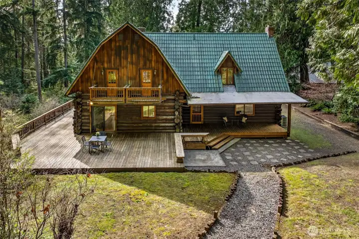 An aerial perspective reveals the remarkable scale of this property's outdoor living — multi-level decks, a private upper balcony, a covered rear porch, and a sweeping green lawn all nestle within a canopy of old-growth Pacific Northwest forest.