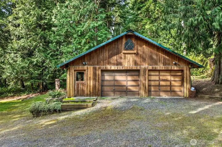 The detached two-car garage is a standout bonus — a beautifully crafted structure with matching green roof trim, a leaded diamond-pane gable window, and a pedestrian door, offering exceptional storage, workshop, or hobby space well beyond what most properties provide.