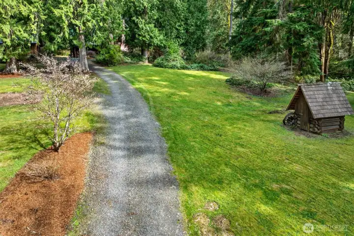 The long private driveway leads through open lawn framed by towering conifers, with a charming decorative log structure adding to the property's storybook character — every inch of these 3.71 acres invites exploration and enjoyment.