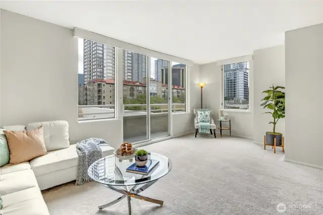 Cheerful living area with access to Juliet balcony and oversized windows for enjoying ample daylight and nighttime city lights.