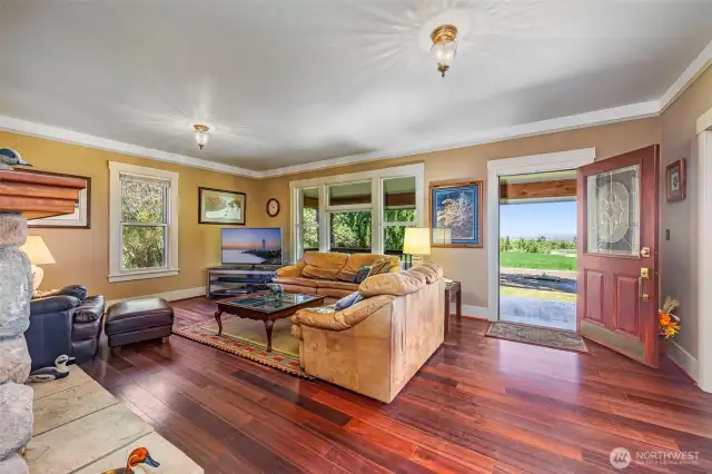 A welcoming space with a view! This angle showcases the refinished 2023 hardwood floors, charming front entry, and seamless flow out to the covered porch—perfect for indoor-outdoor living.