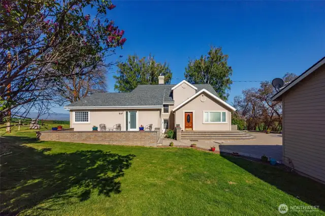 Looking from the shop towards the house, you’ll spot the inviting patio just off the primary suite and the back door leading into the convenient laundry/mud room area—perfect for easy access and seamless living.