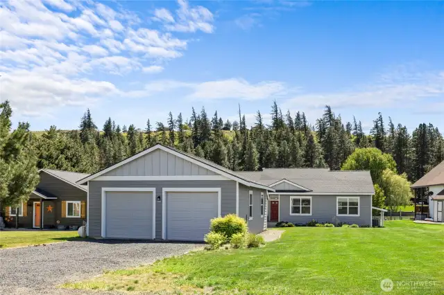 Charming home with gray siding, two-car garage, lush lawn, and a scenic forest backdrop. Great curb appeal!