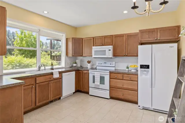Spacious kitchen with wood cabinetry, white appliances, ample counter space, and a bright window overlooking greenery.