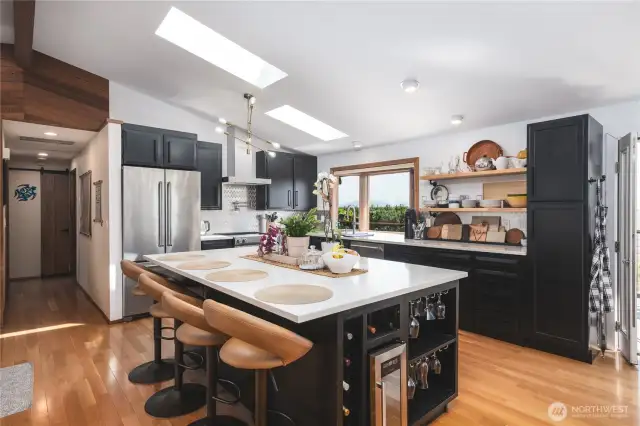 Kitchen with large island with eating space and built-in wine frig, open shelving, stainless appliances and backsplash, quartz counters and vaulted ceilings for that open feel. Light, bright and cheery!