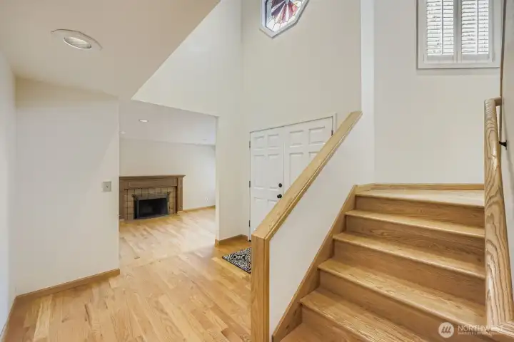 The staircase angles from the front entry, leading you to the upper level. It is brightly lit with soaring ceilings and a wall of windows.