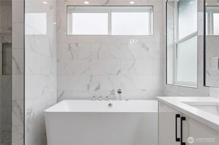 Primary bath jetted soaking tub set against floor-to-ceiling marble tile