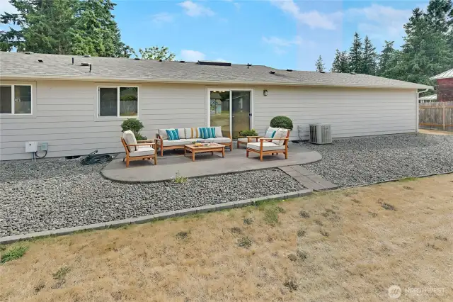 The spacious, fully fenced back yard has a cement patio just outside of the dining room area. Note there's a heat pump for efficient heating and cooling. This photo is virtually staged for your visual enjoyment.