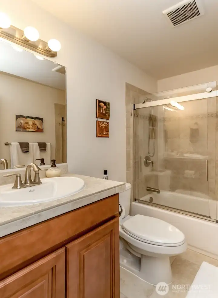 The guest bathroom has tiled floors, countertop and tub surround.