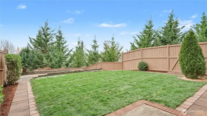 Beautifully landscaped backyard with a grassy area for play and charming pavers for easy access.