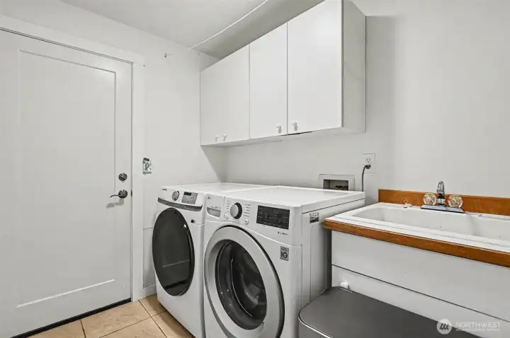 Main level laundry room adjacent to the kitchen and the garage featuring a utility sink.