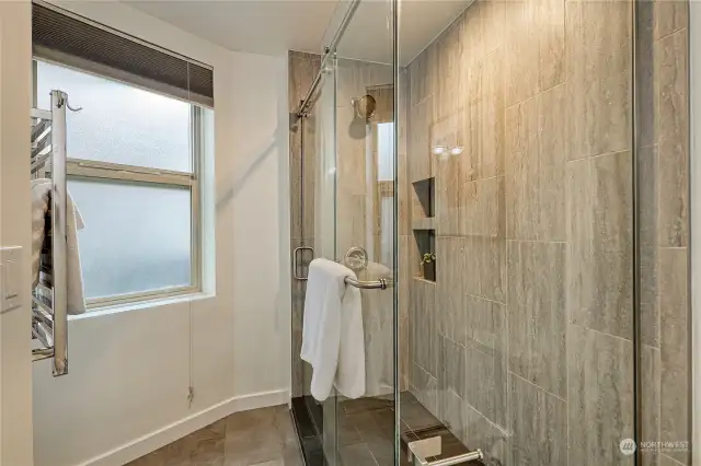 Primary shower with heated towel rack, opening window to bring in fresh air and tile floors