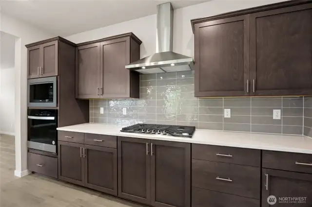 Photo is representational. Actual home is under construction and finishes and paint colors may vary. See site agent for details. Kitchen with quartz countertops, stainless steel appliances, and gas cooktop with gourmet hood vent.