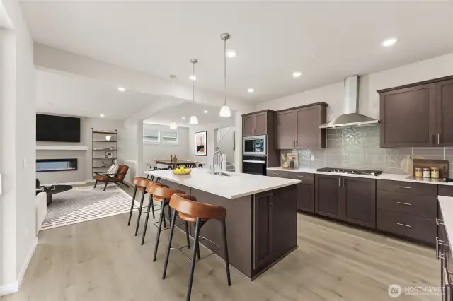 Large kitchen with stainless steel appliances, gourmet cooktop and hood-vent, quartz countertops, pendent lights, and breakfast bar. Photo of actual home with virtual staging.