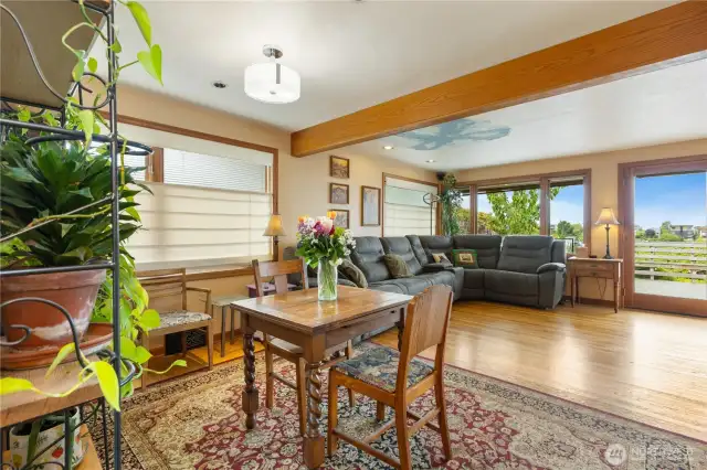 Open-concept living dining room facing large windows w/updated modern lighting and beautiful wood beams and hard wood flooring