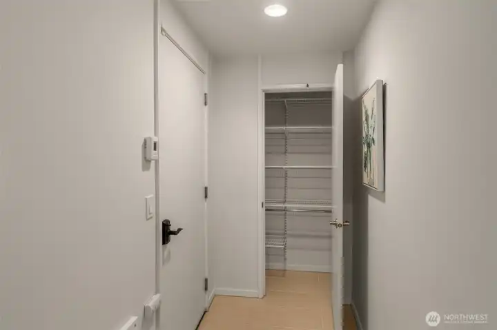 This bright, efficient hallway closet next to garage features clean white walls, ample wire shelving with double hanging rods, a full-length mirrored door (reflected), and a serene abstract artwork accent.
