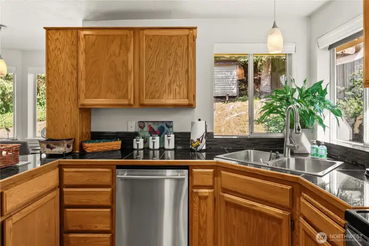 The kitchen features a corner sink with views to the backyard garden,  granite tile counters, and stainless appliances.