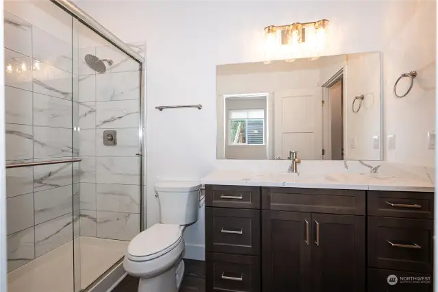 The Guest Bathroom boasts a sizable vanity with gorgeous quartz counters and a full tile shower with a sleek sliding glass door.