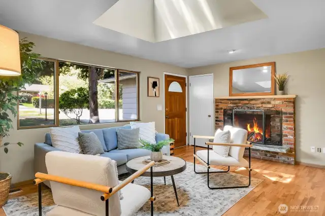 Bright living room with skylight, hardwoods, and a cozy wood-burning fireplace.
