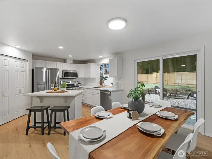 Open remodeled kitchen and dining area featuring white cabinetry, island seating, stainless steel appliances, and sliding door to access the fully fenced backyard