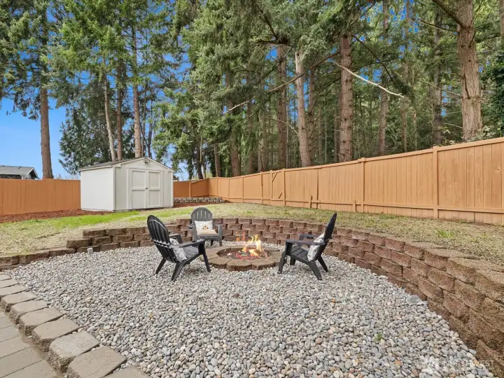 Fully fenced yard with storage shed and wooded backdrop