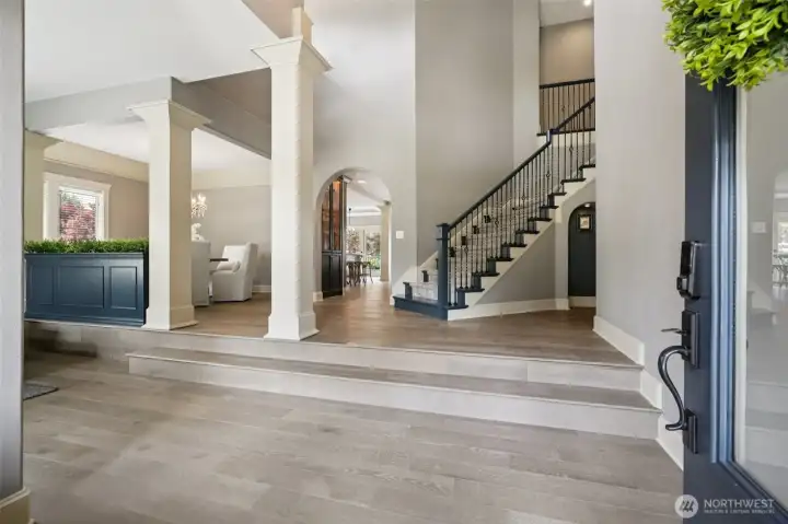 Welcoming front entry showcasing a grand foyer with tall ceilings, architectural columns, and a statement staircase. Wide-plank flooring and an open sightline into the main living areas create a refined first impression and seamless flow throughout the main level.