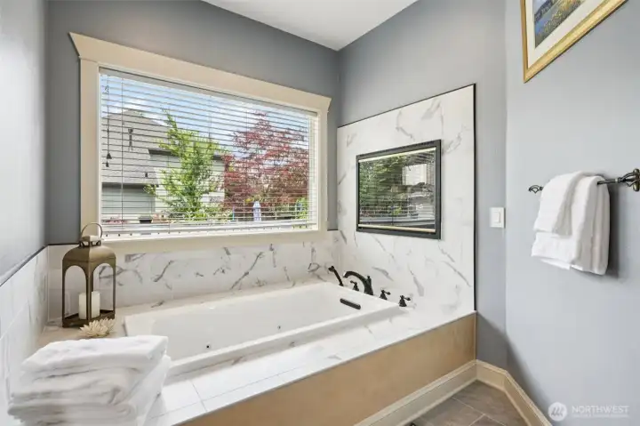 Primary bathroom featuring a jetted soaking tub complemented by a double-sided fireplace, creating a warm and relaxing atmosphere. Thoughtful finishes, natural light, and a spacious layout enhance both comfort and functionality.