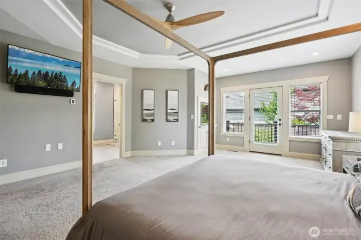 Expansive primary bedroom suite featuring plush carpeting, tray ceiling, ceiling fan, and abundant natural light. French doors provide direct access to the private deck, creating a seamless connection to outdoor living and enhancing the overall sense of space and comfort.