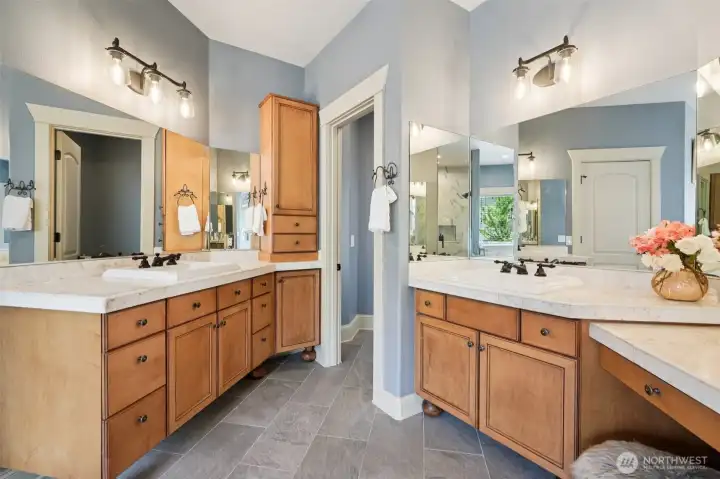 Primary bathroom featuring dual vanities with solid-surface countertops, abundant cabinetry, and coordinated lighting. The spacious layout offers excellent functionality, generous storage, and a comfortable separation of space for everyday use.