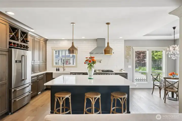 Open-concept kitchen centered around a large island with seating, quartz countertops, and custom cabinetry. The space flows seamlessly into the dining and living areas, enhanced by pendant lighting, wood flooring, and abundant natural light—ideal for everyday living and entertaining.