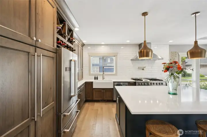 Chef-inspired kitchen showcasing custom appliance cabinetry with integrated wine storage, farmhouse sink, quartz countertops, and a professional-grade cooking area. Thoughtful layout, quality finishes, and abundant storage enhance both everyday functionality and entertaining appeal.