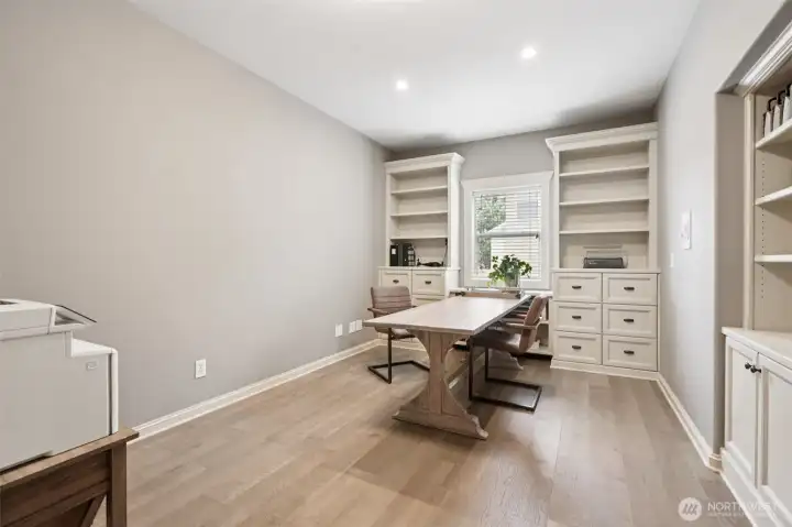 Lower-level office featuring custom built-in shelving and cabinetry, wood flooring, and recessed lighting. This quiet, well-designed workspace offers excellent flexibility for remote work, study, or creative use, with ample storage and a comfortable layout.