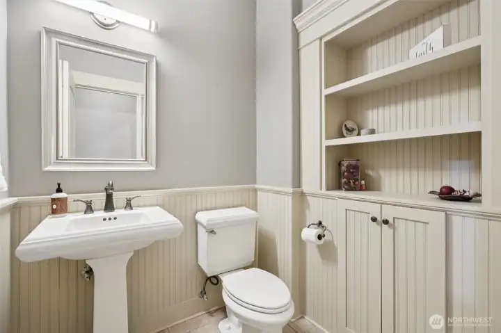 Convenient lower-level half bath featuring built-in shelving, classic pedestal sink, and neutral finishes. Ideally located near the laundry and lower-level living areas, offering comfort and practicality for guests and everyday use.