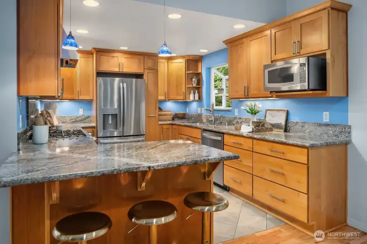 This well-appointed chef's kitchen offers granite countertops, rich custom cabinetry, stainless steel appliances, and a generous island with bar seating — thoughtfully designed with abundant storage and workspace for the home cook.
