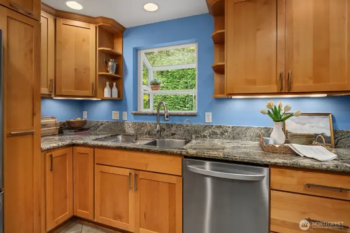 A bright garden window over the sink fills this thoughtfully designed kitchen with natural light, complementing the granite counters, custom tile backsplash, and warm cabinetry for a inviting and functional workspace.
