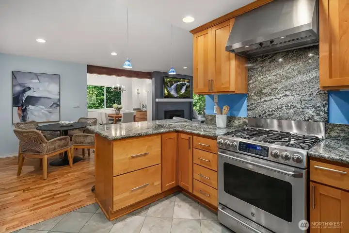 A premium stainless steel range with professional hood, granite counters, and a functional center island make this kitchen a true chef's dream — all flowing seamlessly into the open living and dining spaces beyond.