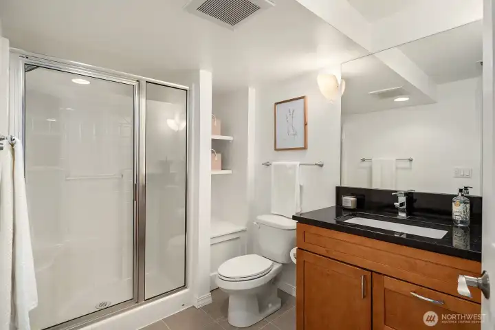 The conveniently located lower level bath features a walk-in shower, classic vanity with dark countertop, and clean finishes, providing comfortable and functional facilities for the lower level bedrooms and guests.